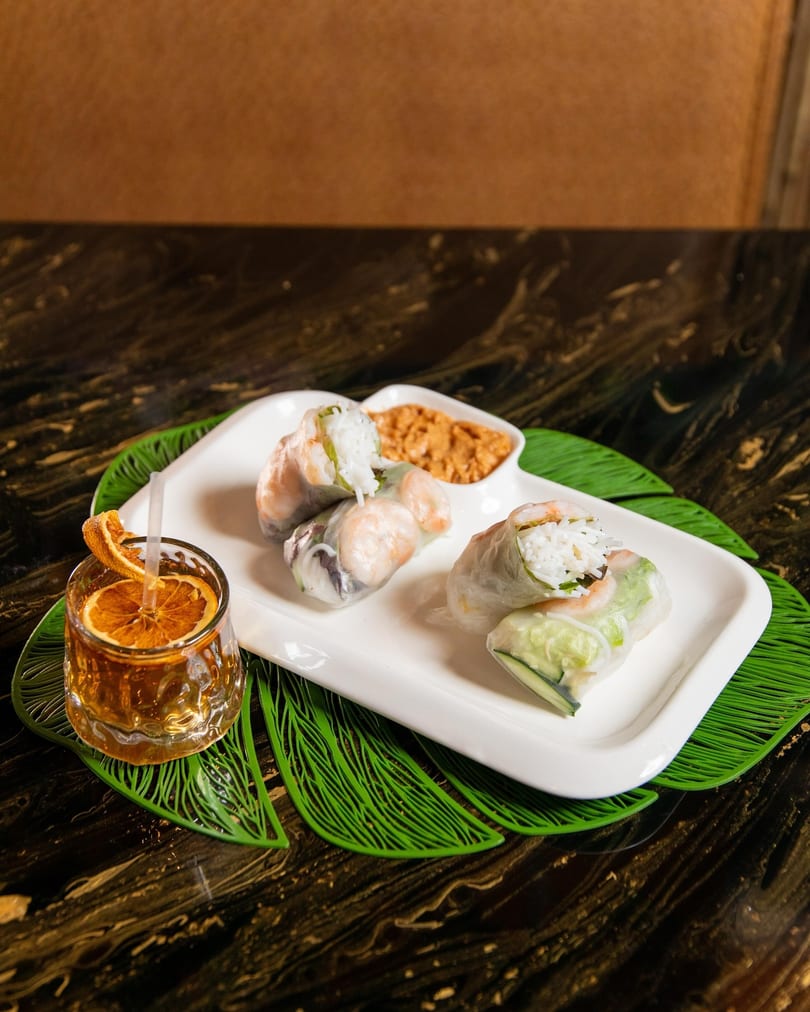 Shrimp and rice spring rolls with peanut sauce and a cocktail garnished with dried orange.