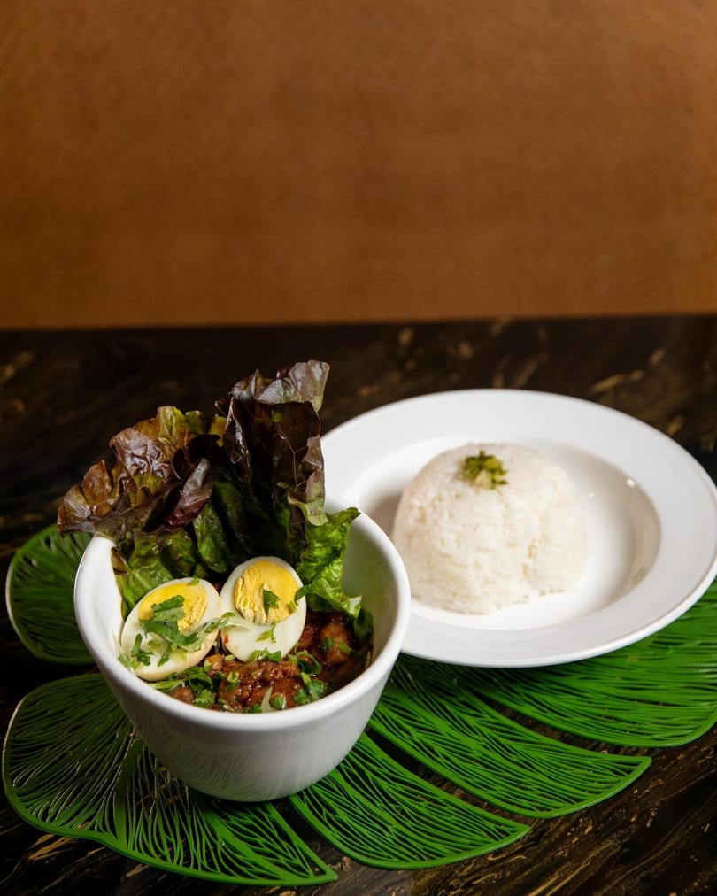 A bowl of stew with lettuce and hard-boiled eggs, served with a side of white rice.